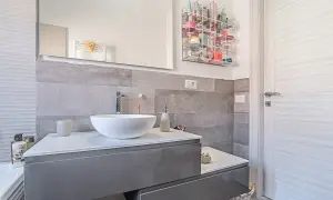 Bagno moderno grigio e legno con lavabo bianco, specchio e porta in legno chiaro. Organizzatore trasparente pieno di cosmetici.