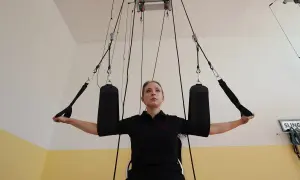 Kobieta ćwiczy z użyciem systemu podwieszeń, wykonując ćwiczenie angażujące mięśnie w sposób przypominający skurcz izotoniczny.