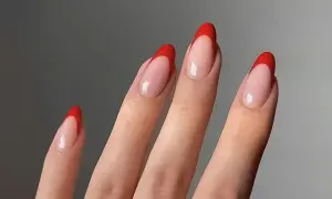 Dłonie z paznokciami w kształcie migdałków, ozdobione klasycznym french manicure z intensywnie czerwonymi końcówkami.