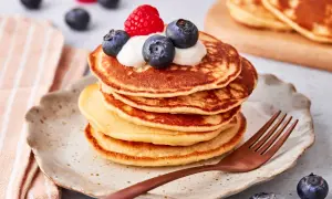 Ein Stapel goldbrauner Pancakes mit Joghurt, Blaubeeren und einer Himbeere obendrauf. Ein köstlicher pancake mit joghurt für ein perfektes Frühstück.
