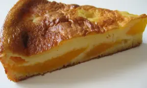Tranche de clafoutis aux pêches, dorée et moelleuse, avec des morceaux de fruits juteux.