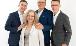 Cztery osoby w eleganckich strojach, uśmiechnięte, na białym tle.