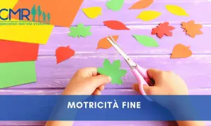 Mano di bambino che ritaglia forme di foglie colorate con forbici rosa, un'attività che stimola la motricità fine.