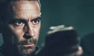 Sebastian Stakset i en intensiv scen från en film. Hans blick är fokuserad, kanske på ett manus eller en motspelare.