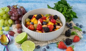 Ein bunter, sommerlicher Obstsalat mit Beeren, Trauben und Mango, garniert mit Minze und Limettenspalten.