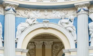 Barokowe stiuki: rzeźby kobiet, gryfy i ornamenty na tle błękitnej ściany.