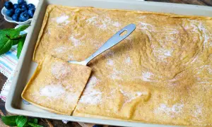 Ein frisch gebackener Ofenpfannkuchen, bestreut mit Zucker und Zimt, wartet darauf, serviert zu werden. Ein Stück ist bereits herausgeschnitten.