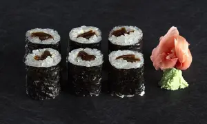 Sześć kawałków sushi z ryżem i ciemnym nadzieniem, obok różowy imbir i zielone wasabi.