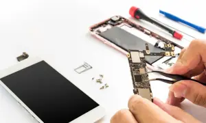 Naprawa telefonu: dłonie trzymające płytę główną, obok rozebrany smartfon i narzędzia.