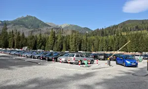 Duży, kamienisty morskie oko parking pełen samochodów, otoczony gęstym lasem świerkowym i górami.