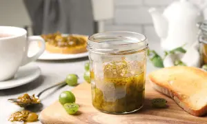 Ein Glas stachelbeermarmelade steht neben geröstetem Brot und frischen Stachelbeeren. Perfekt zum Frühstück oder als Brotaufstrich.