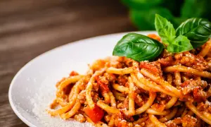 Talerz spaghetti z sosem bolońskim, posypany parmezanem i udekorowany bazylią.