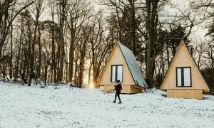 Deux tiny houses à l'année dans un paysage enneigé, entourées d'arbres. Une personne marche dans la neige.