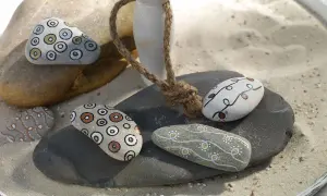 Ideas para pintar piedras de playa: piedras decoradas con círculos concéntricos y líneas onduladas en tonos tierra y blanco.