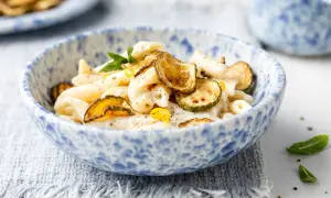Piatto di pasta cremosa con ricotta e zucchine croccanti, guarnito con scorza di limone e menta.