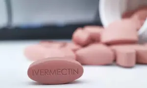Różowe tabletki z napisem "IVERMECTIN" rozsypane z białego pojemnika.