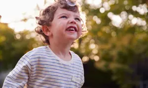Uśmiechnięte 3 letnie dziecko z kręconymi włosami łapie bańkę mydlaną w słoneczny dzień.