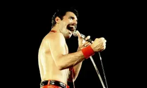 Freddie Mercury w czerwonych spodniach i opasce na nadgarstku śpiewa do mikrofonu. Nawet jako dorosły, jego energia przypominała dzikie dziecięce zabawy.