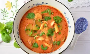 Aromaticzna zupa tom yum z kurczakiem, grzybami i kolendrą, podana w ozdobnej misce.