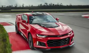 Czerwone Camaro ZL1 z czarnymi pasami na masce i dachu pędzi po torze wyścigowym, zostawiając za sobą smugę.