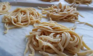 Domowy przepis na makaron do rosołu. Świeże, żółte nitki makaronu ułożone na papierze do pieczenia, gotowe do suszenia.