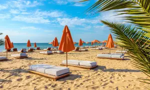 Słoneczny dzień na plaży z pomarańczowymi parasolami i leżakami na złotych piaskach.