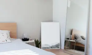 Jasne, minimalistyczne lustro w sypialni feng shui odbija łóżko i tworzy wrażenie większej przestrzeni.