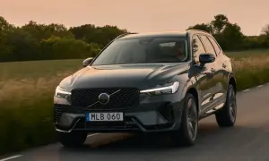 Ciemnoszary Volvo XC60 2025 jedzie drogą wśród zieleni o zachodzie słońca.