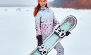 Uśmiechnięta dziewczyna w czapce i kurtce z kwiatowym wzorem trzyma **co to jest snowboard** z kolorowymi zdobieniami.