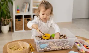 Mała dziewczynka bawi się fasolkami i makaronem. Wspaniałe zabawy sensoryczne dla rocznego dziecka, rozwijające jego ciekawość i zdolności manualne.