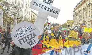 Manifestantes protestan contra el fraude de ley y el abuso de temporalidad, exigiendo fijeza. Un cartel en forma de cruz dice "RIP INTERINOS", reflejando el deseo de no ser interino toda la vida.