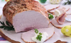 Soczysta szynka pieczona w rękawie, pokrojona w plastry, z chrzanem i natką pietruszki. Idealna na wielkanocny stół.