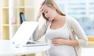 Kobieta w ciąży z bólem głowy i dłonią na brzuchu, martwiąca się o arytmię w ciąży.