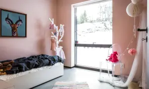 Ein gemütliches Kinderzimmer mit einer rosa Wand, einem Bett, Spielzeug und einem großen Fenster mit Blick auf eine verschneite Landschaft.