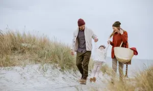 Radosna rodzina spaceruje po plaży. Piękna jesień nad morzem, wiatr rozwiewa włosy, a dziecko radośnie kręci się w powietrzu.