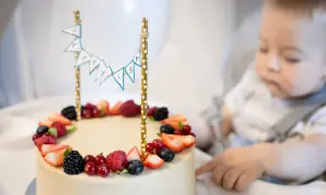 Uroczy tort na pierwsze urodziny, ozdobiony owocami i chorągiewkami z napisem "Sto lat".
