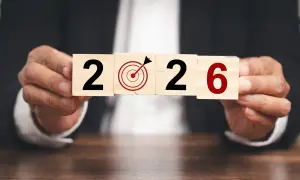 Ręce trzymają kostki z napisem "2026" i tarczą celowniczą. To symboliczne przedstawienie celów i planowania, jak środki trwałe co to, w kontekście przyszłości.