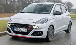 Biały Hyundai i10 N Line w ruchu, z widoczną kratką i światłami LED. Sprawdź aktualną hyundai i10 cena.