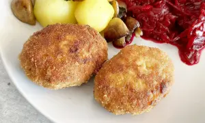 Dwa złociste kotlety mielone z indyka, podane z ziemniakami, grzybami i buraczkami.