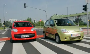 Czerwony i zielony samochód na pasach. Czy w terenie zabudowanym można wyprzedzać? Znak zakazu wyprzedzania jest kluczowy.