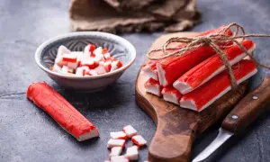 Paluszki surimi, czyli co to jest? Kilka sztuk związanych sznurkiem na desce, obok miseczka z pokrojonymi kawałkami i pojedynczy paluszek.