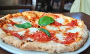 Une délicieuse margarita pizza, avec sa croûte dorée, sa sauce tomate vibrante et son fromage fondant, garnie de feuilles de basilic frais.