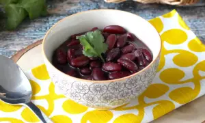 Un bol de haricot rouge savoureux, garni d'une feuille de coriandre, sur une serviette jaune à pois.
