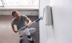 Mężczyzna maluje ścianę na biało. Wybór odpowiedniej farby do ścian jest kluczowy dla efektu.
