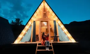 Soirée de camping nature corse. Une femme assise sur les marches d'un chalet en bois illuminé par des guirlandes lumineuses, profitant de la nuit.