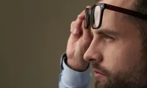 Mężczyzna z dużą wadą wzroku poprawia okulary.