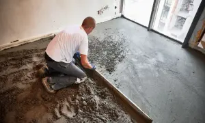 Budowlaniec klęczy, wyrównując świeży jastrych za pomocą łaty.