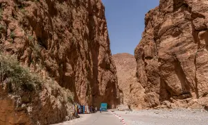Die Todra-Schlucht mit ihren steilen, roten Felswänden. Eine Straße führt hindurch, gesäumt von Souvenirständen und einem blauen LKW.