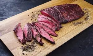 Perfekt zubereitetes Skirt Steak, in Scheiben geschnitten, liegt auf einem Holzbrett. Gewürze und Pfeffer sind verstreut.