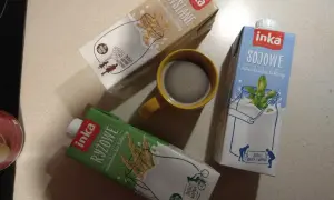 Trzy kartony napojów Inka (owsiane, sojowe, ryżowe) i kubek kawy.